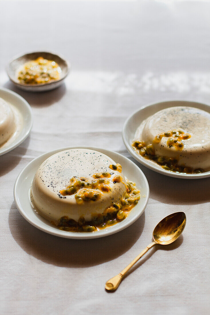 Panna Cotta mit Passionsfrüchten, serviert auf einem Teller mit einem goldenen Löffel