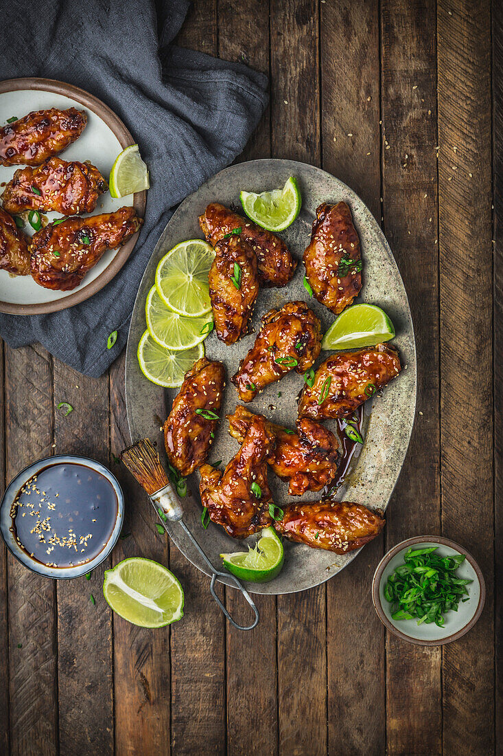 Glazed chicken wings on metal plate and serving platter with lime, sauce and spring onions