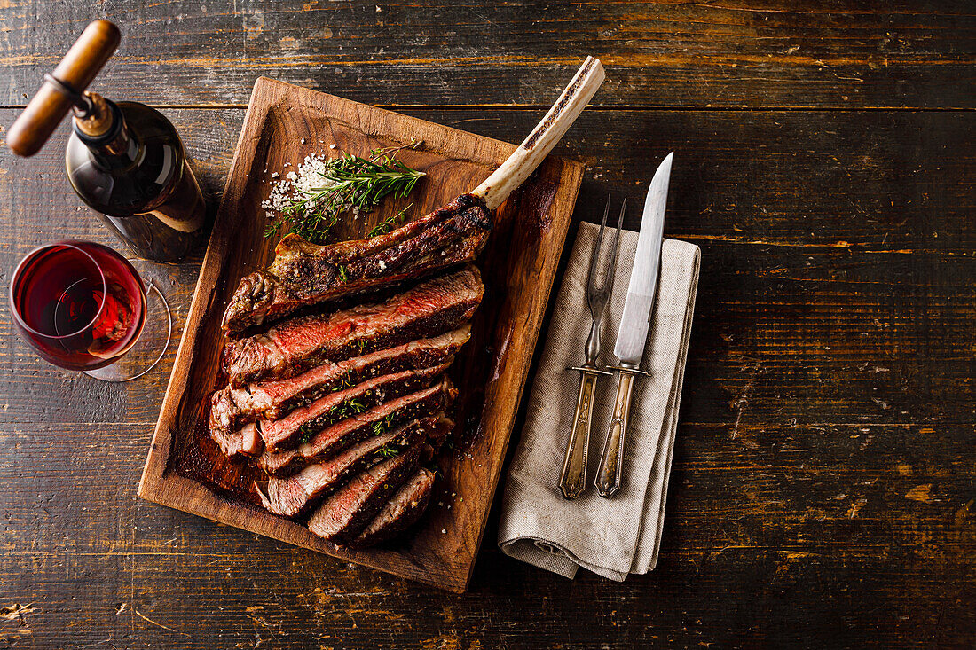Grilled sliced Tomahawk Steak on bone and glass of Red wine on wooden background