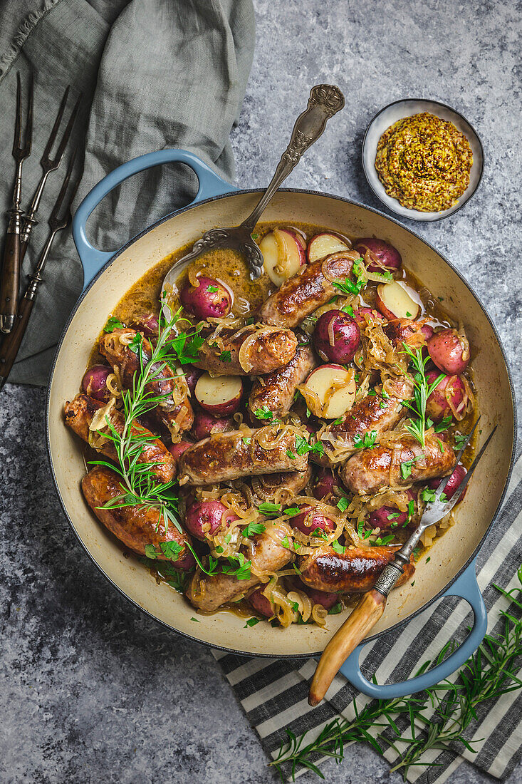 Top view of braised sausage and potatoes in a Dutch oven with mustard in a small bowl