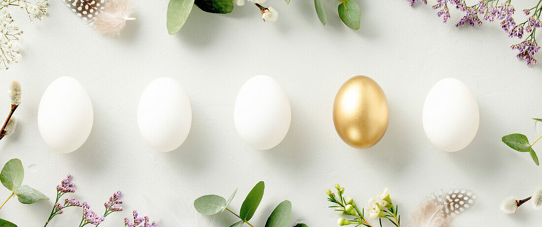 Easter decoration. Happy Easter concept with golden Easter eggs, feathers and spring flowers on a blue background. Flat lay banner