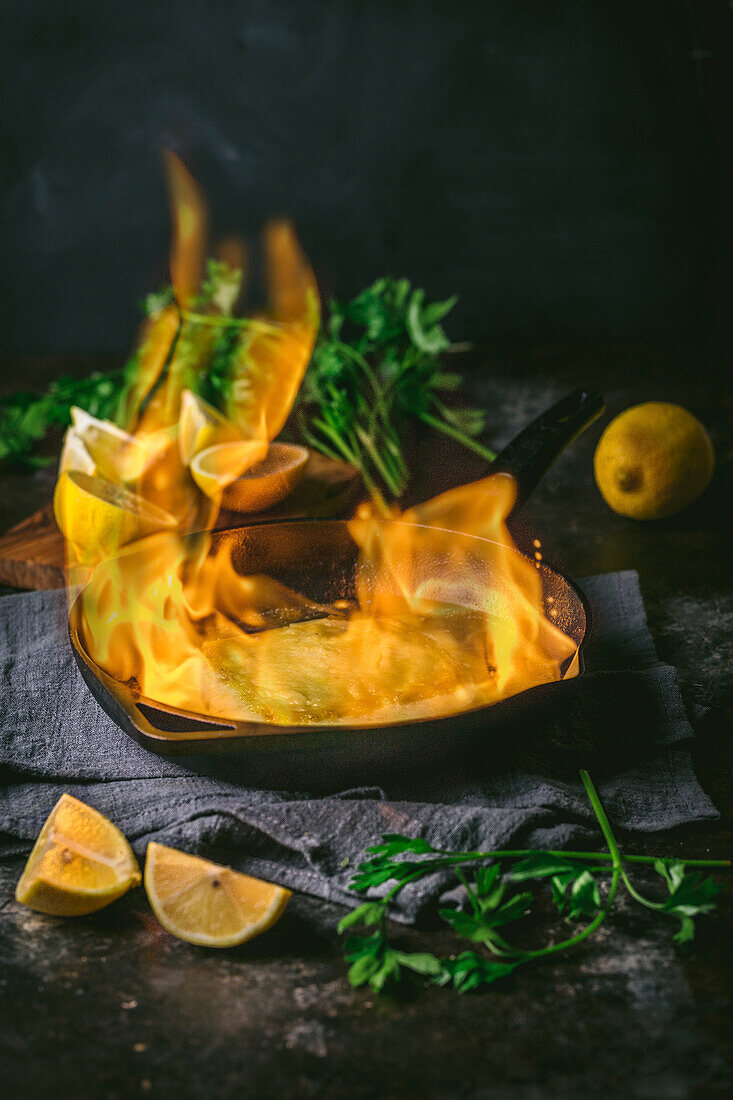 Cheese Flambé with large flame in cast iron skillet with parsley and lemons