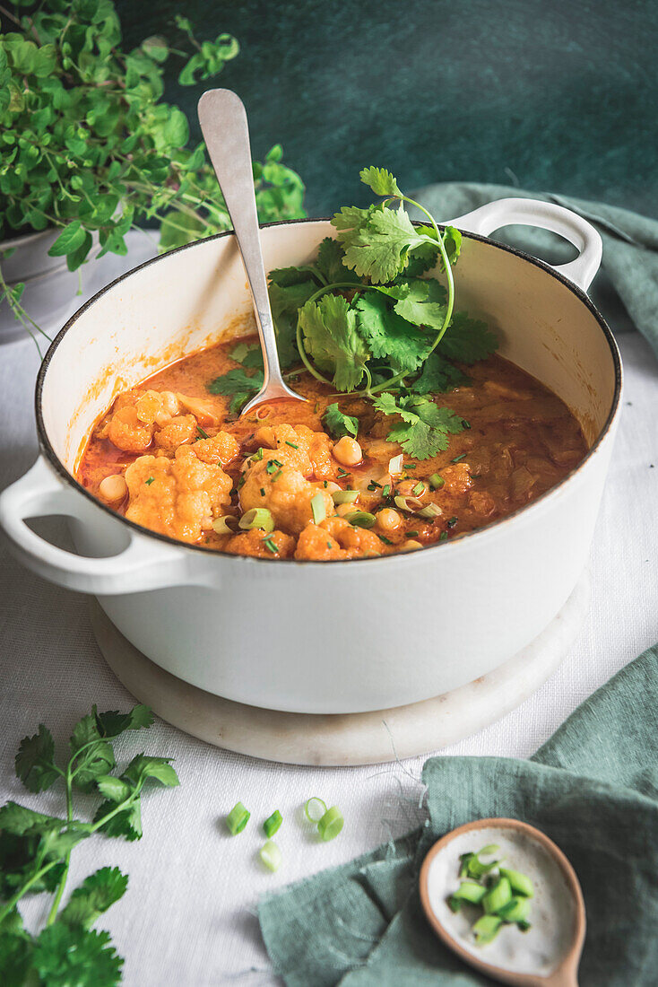 Cauliflower and chickpea curry in a large pan, served with herbs