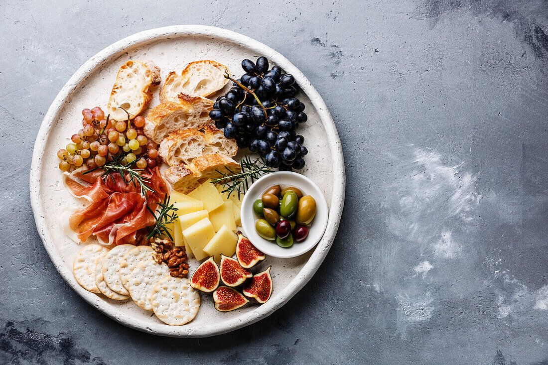 Italian snacks food with ham, olives, cheese, grapes, sausage and bread on concrete background copy space
