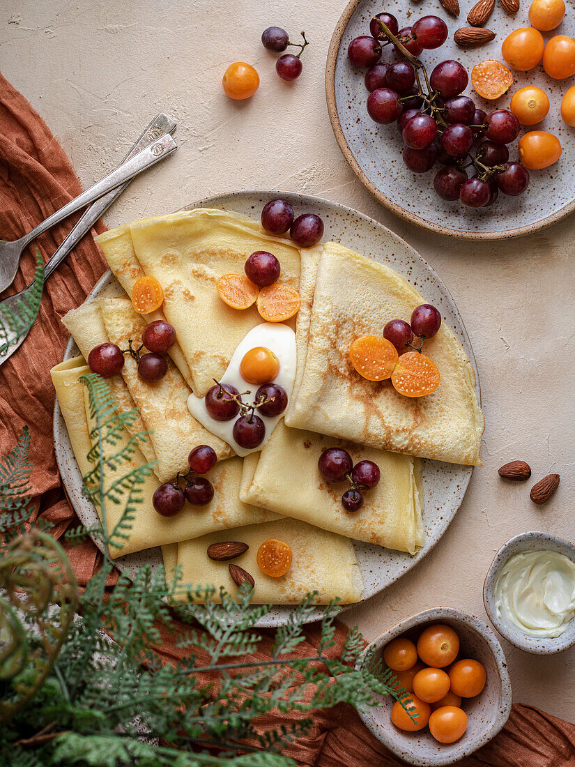 Crepes on a plate served with whipped cream, red grapes and golden berries