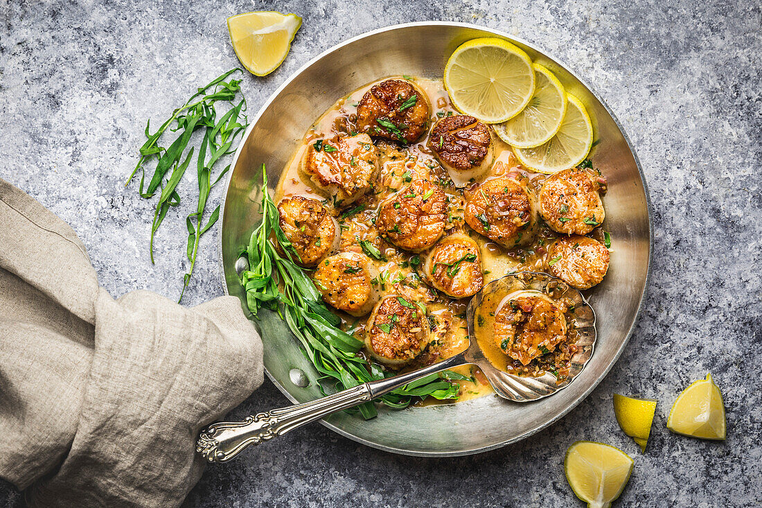 Gebratene Jakobsmuscheln mit brauner Buttersauce in der Pfanne mit Estragon und Zitrone, mit Leinenserviette