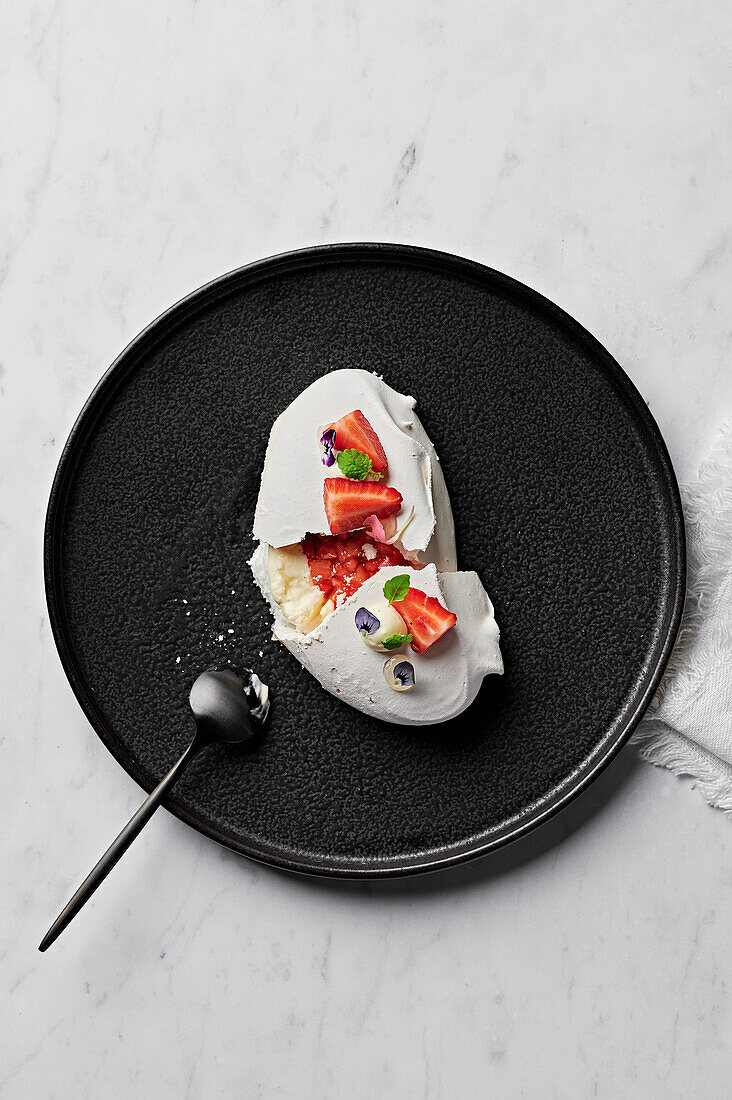 Meringue with yoghurt mousse, macerated strawberries and bergamot gel from above on black plate