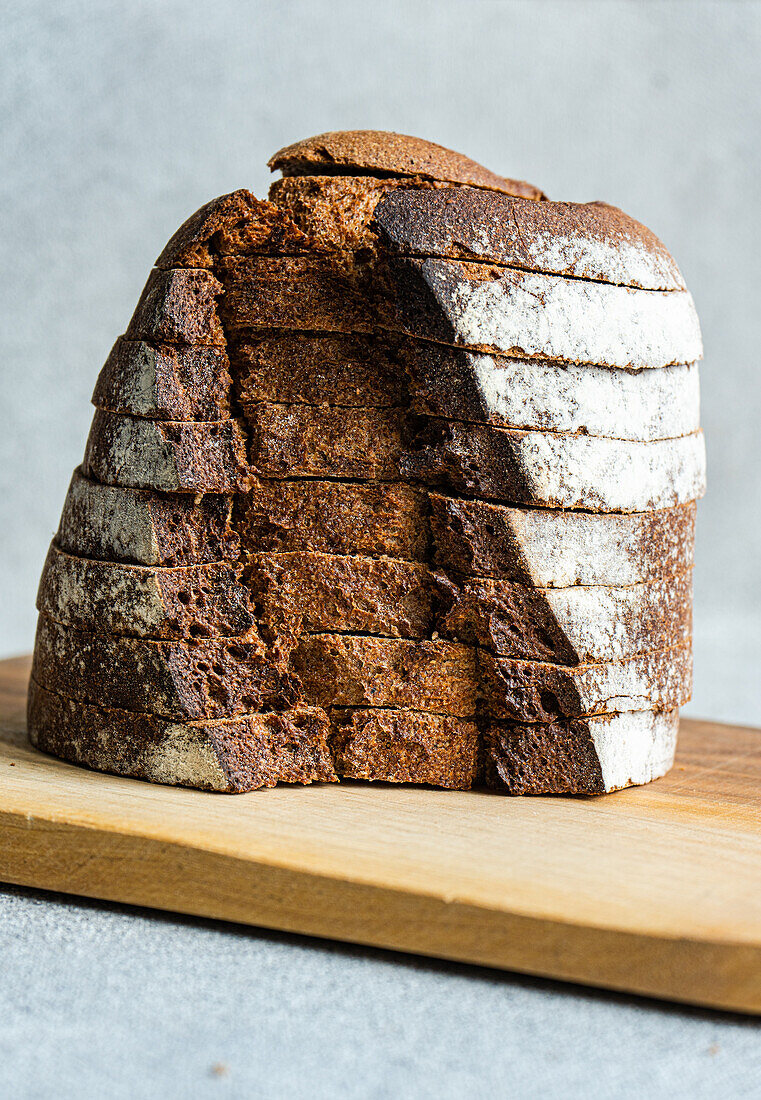 Front view of a stack of rye bread slices on a wooden chopping board against a blurred light-coloured background