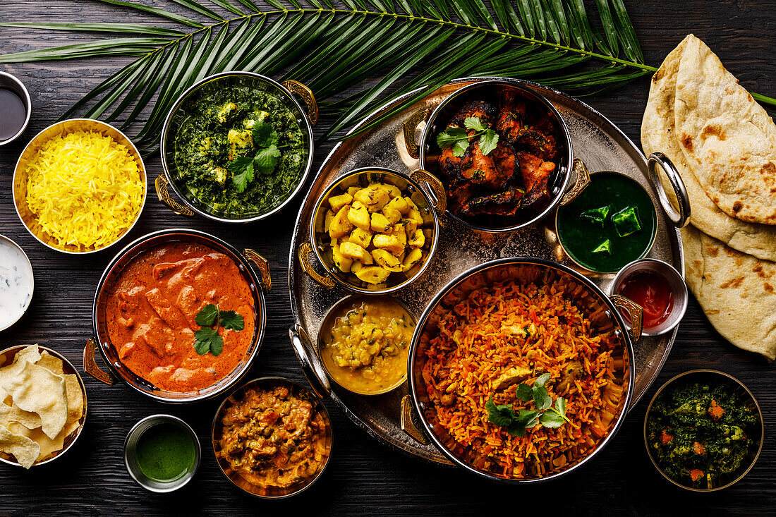 Indian food Curry butter chicken, palak paneer, chiken tikka, biryani, vegetable curry, papad, dal, palak sabji, jira alu, rice with saffron on a dark background