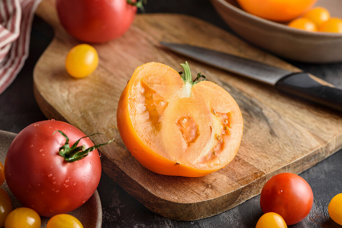 Half a tomato on a chopping board. Nearby are various yellow and red tomatoes