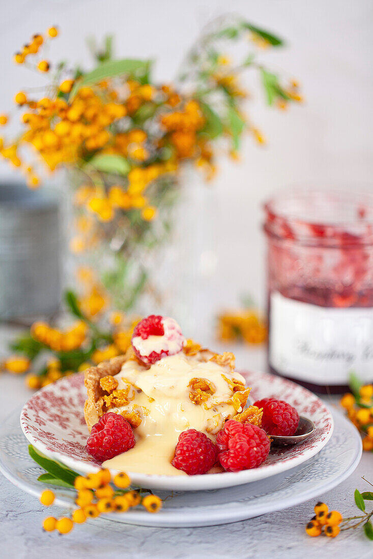 A slice of cornflake cake and fresh raspberries, served on a plate with pudding on top