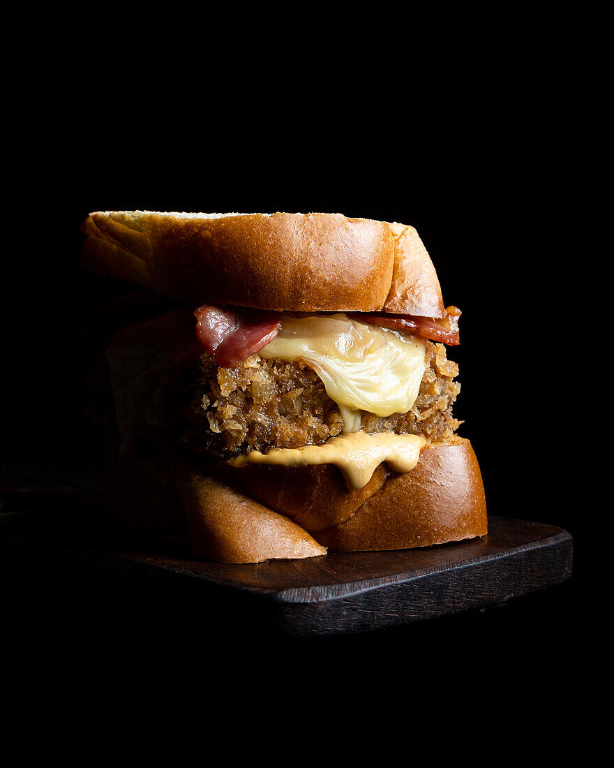 Appetising burger with fresh buns and cheese served on a wooden board on a black background