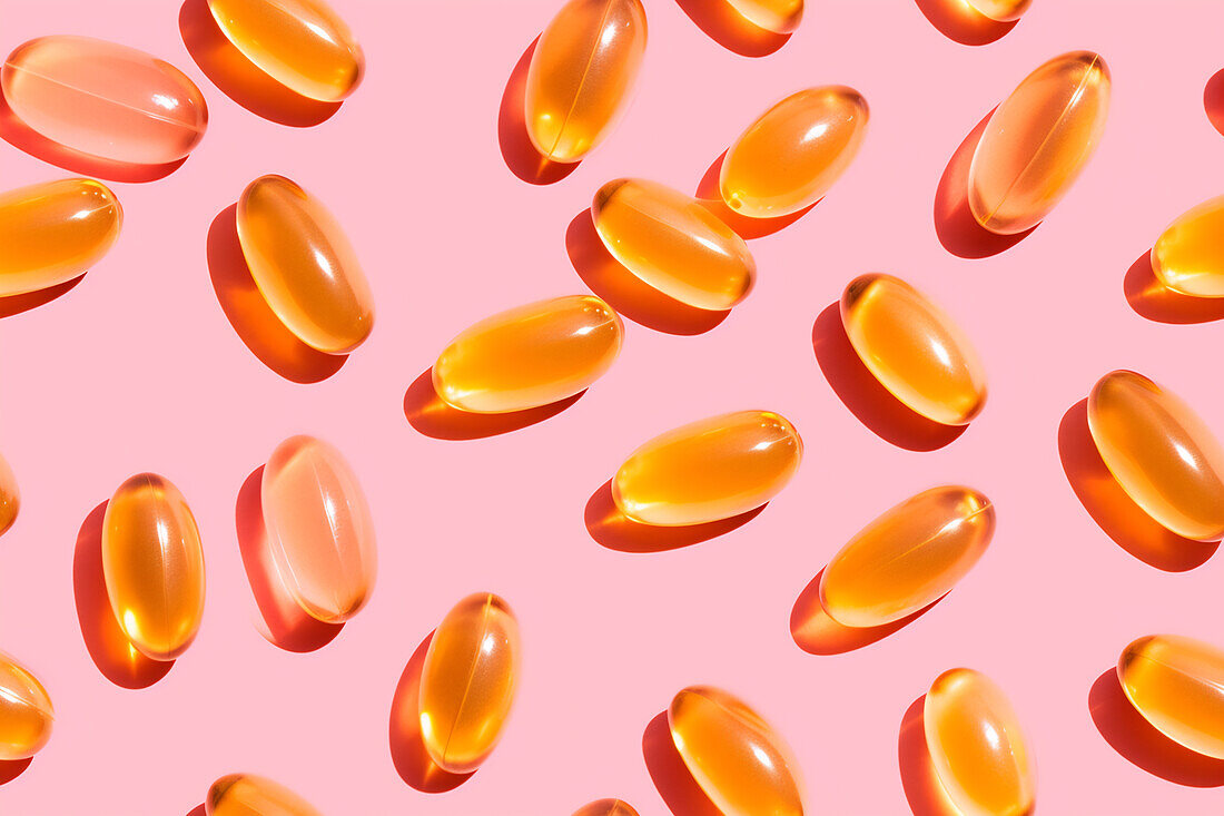 Assortment of orange vitamin pills scattered on a pink background in a bright studio