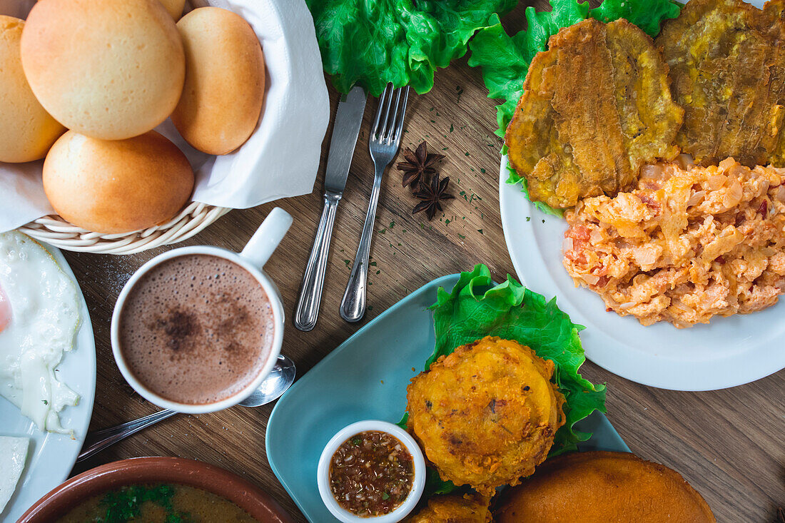 Draufsicht auf eine Reihe appetitlicher kolumbianischer Gerichte mit papas rellenas pan de bono chicharron bunuelos und caldo de costilla mit verschiedenen Getränken auf einem Holztisch in einem Restaurant