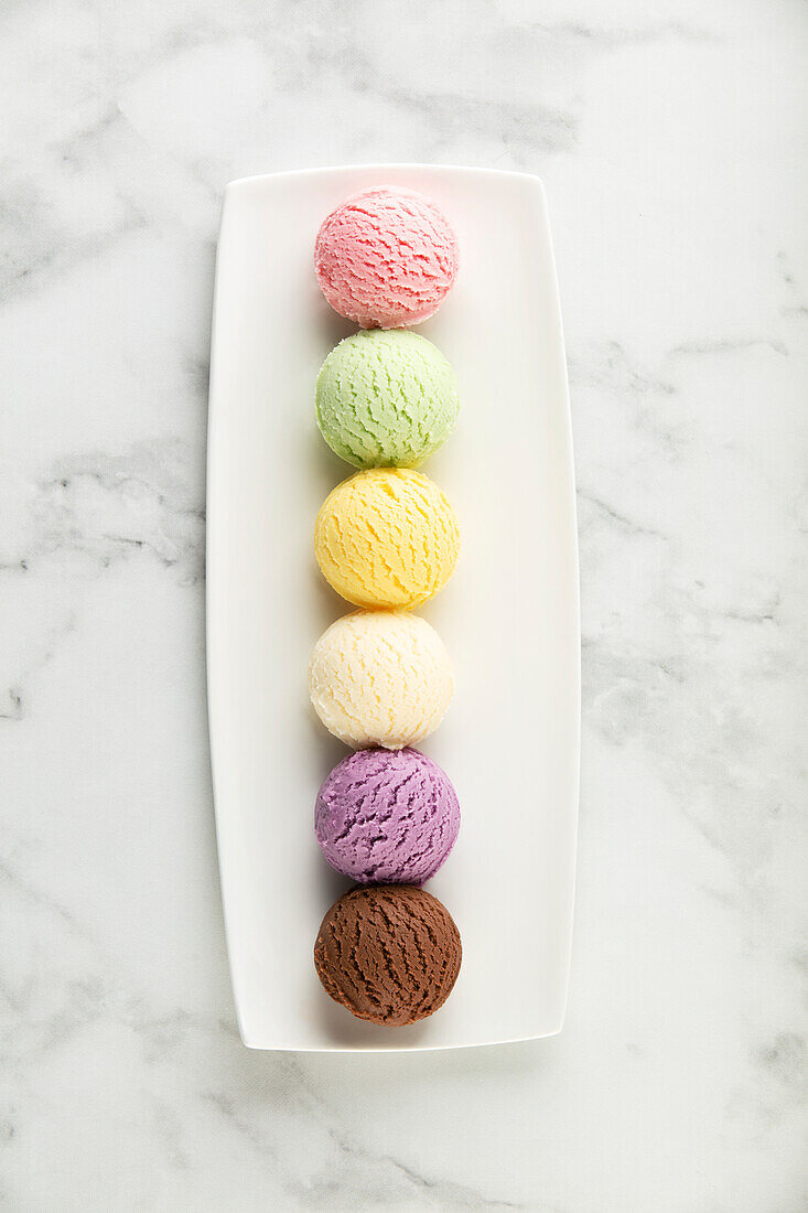 Set of different ice-cream scoops on a white marble background. Strawberry, pistachio, mango, vanilla, blueberry and chocolate ice cream. Top view, laid flat
