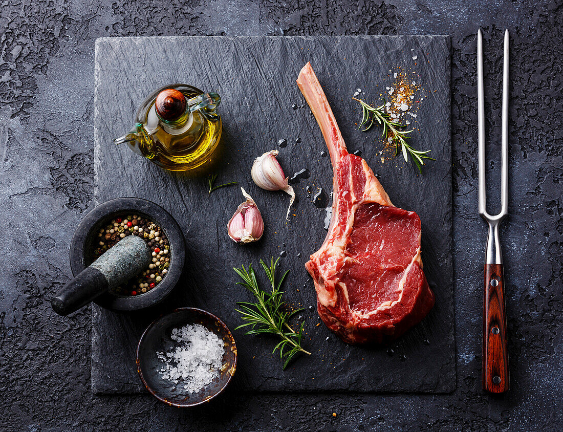 Rohes frisches Kalbsrippensteak mit Knochen und Gewürzen auf dunklem Hintergrund