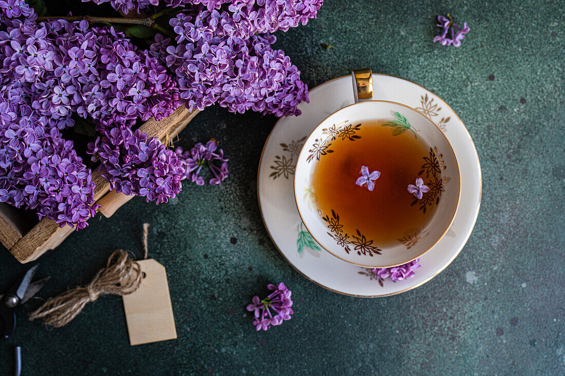 Delicious black tea in a vintage white cup on a mint green concrete table with aromatic lilac flowers