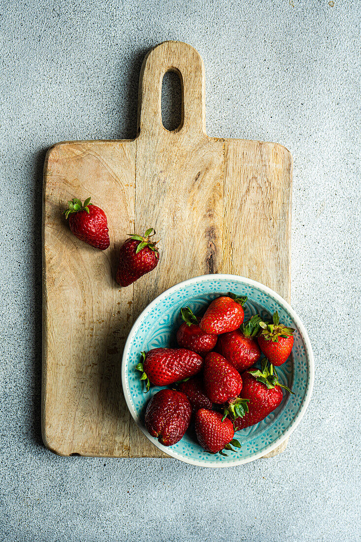 Ripe organic strawberries in a ceramic bowl on a concrete background