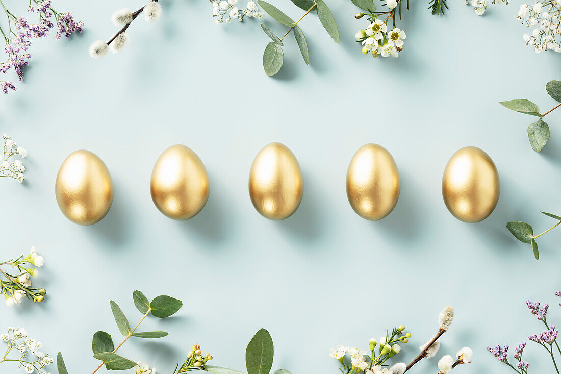Easter decoration. Happy Easter concept with golden Easter eggs, feathers and spring flowers on a blue background. Flat lay banner