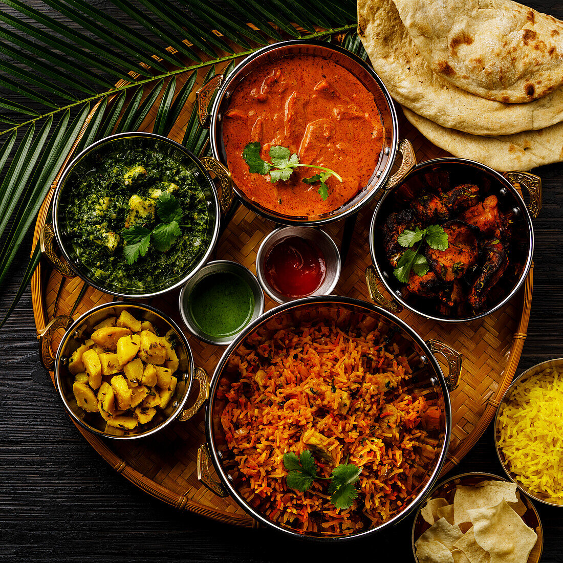 Indisches Essen Curry-Butterhähnchen, Palak Paneer, Chiken Tikka, Biryani, Gemüsecurry, Papad, Dal, Palak Sabji, Jira Alu, Reis mit Safran auf dunklem Hintergrund
