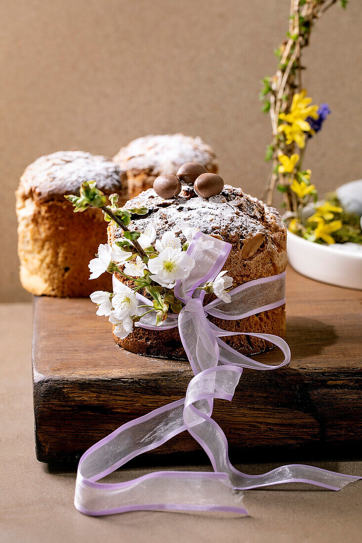 Homemade Italian traditional Easter panettone cakes, decorated by chocolate eggs, pink ribbon and blossoming cherry tree flowers standing on wooden table. Traditional Easter European bake.