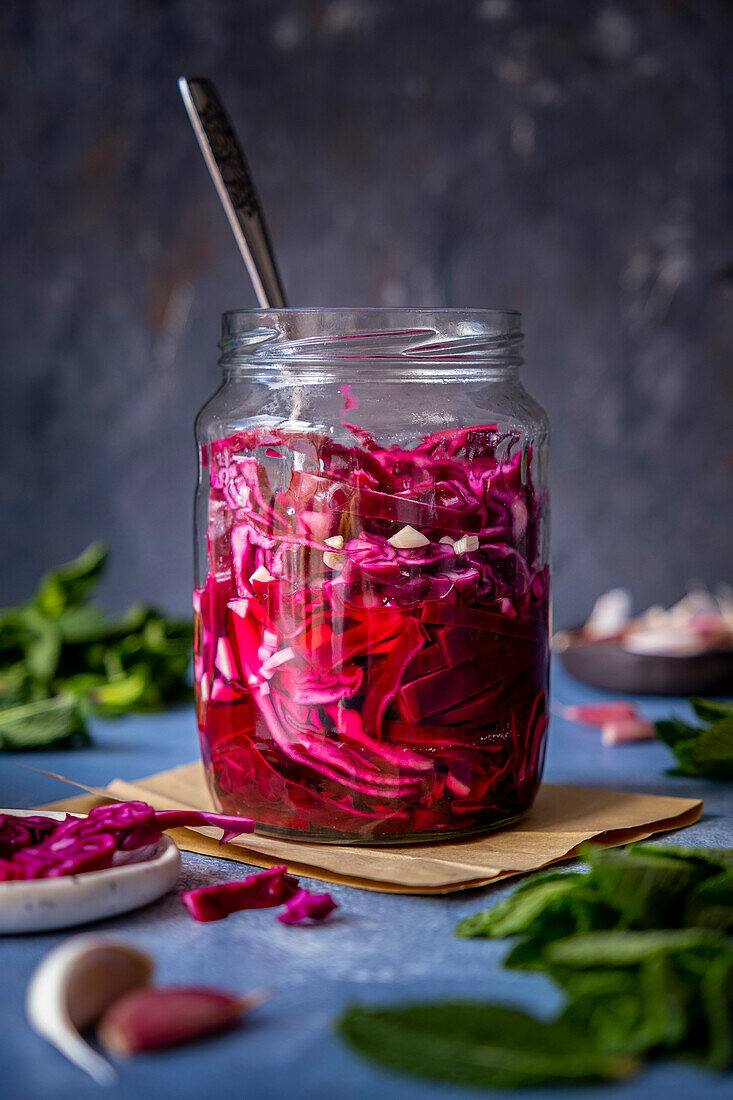 Ein Glas mit eingelegtem Rotkohl und einer Gabel darin, fotografiert vor einem dunklen Hintergrund