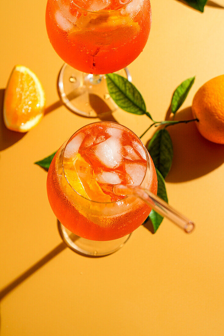 Aperol Spritz Cocktail mit Eis, ein beschlagenes erfrischendes Getränk, auf einem orangefarbenen Hintergrund, Sonnenlicht, Schatten, ein Sommergetränk in einem Weinglas