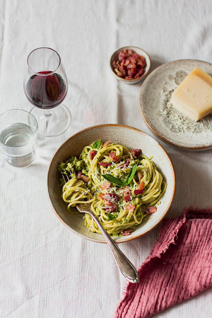 Bowl of spaghetti with basil, pancetta and parmesan, served with a glass of red wine and water