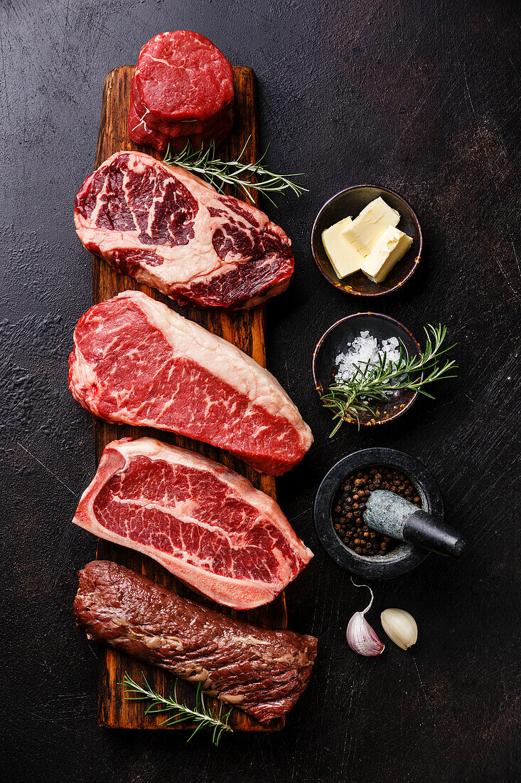 Variety of Raw Black Angus Prime meat steaks Machete, Blade on bone, Striploin, Rib eye, Tenderloin fillet mignon on wooden board and seasoning
