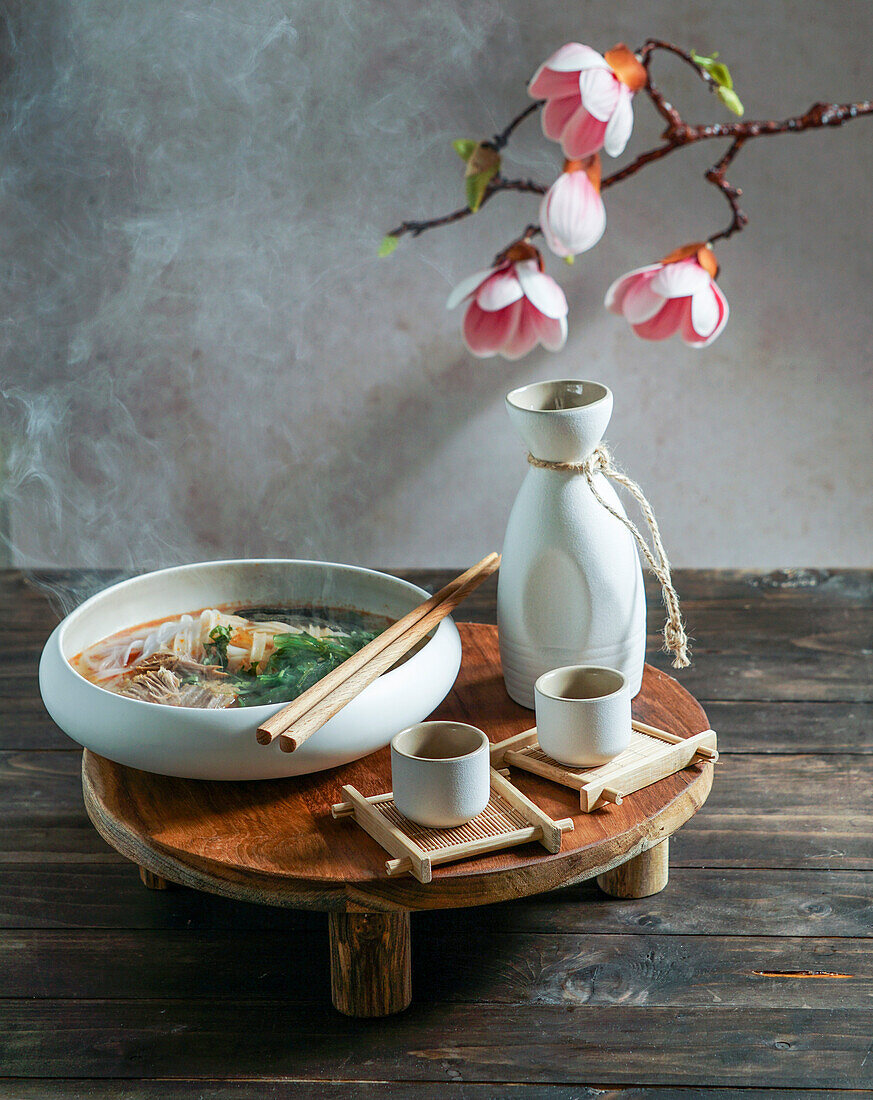 Japanese sake composition with Asian soup with rice noodles, Asian food ceremony with magnolia blossoms