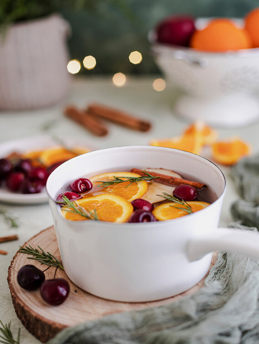Weihnachtspunsch mit Kirschen, Orangen und Rosmarin, in einem weißen Topf