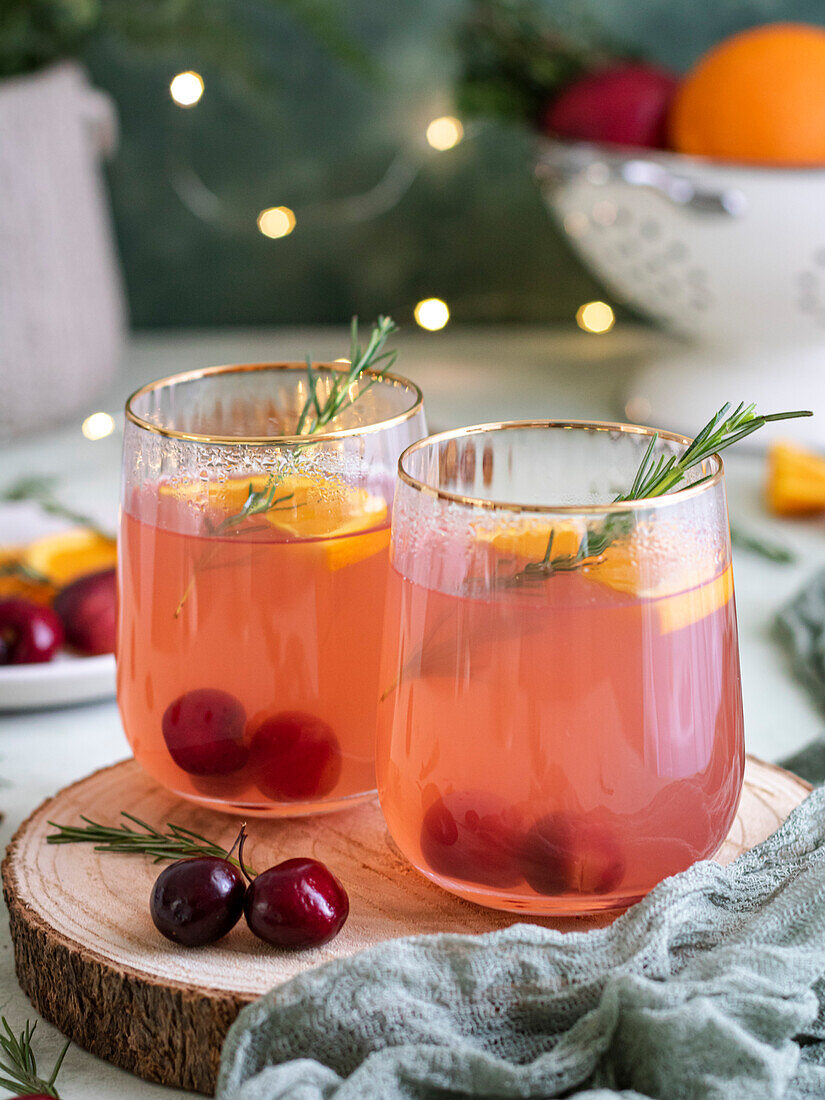 Weihnachtspunsch in Gläsern, dekoriert mit frischen Kirschen, Orange und Rosmarin