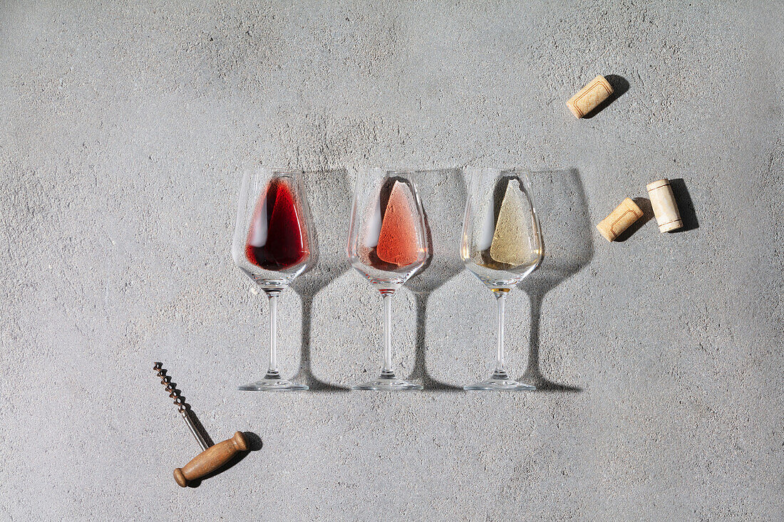 Weinkomposition mit Rot-, Rosé- und Weißwein in Gläsern, schönes Sonnenlicht und Schatten auf grauem Hintergrund. Draufsicht, flach gelegt. Weinbar, Weingut, Weindegustation Konzept. Minimalistische trendige Fotografie