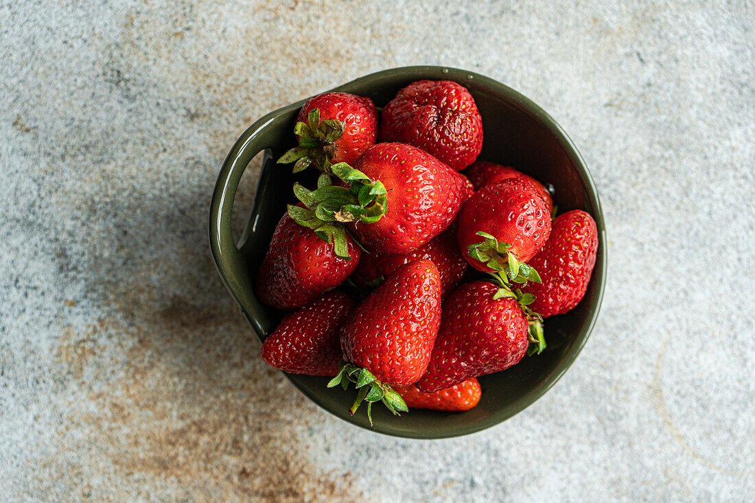 Ripe organic strawberries in a ceramic bowl on a concrete background