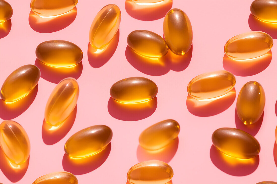 Assortment of orange-coloured vitamin pills scattered on a pink background in a bright studio