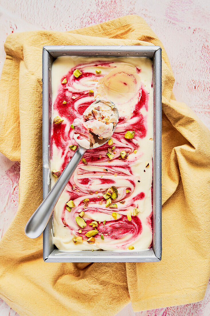 Raspberry ripple sundae with pistachios on a pink background with a yellow napkin