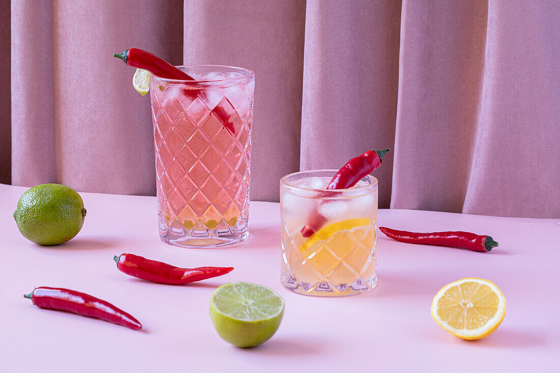 Transparente Gläser, gefüllt mit kalten, erfrischenden Cocktails, serviert mit Chilischoten und Eiswürfeln, auf einem Tisch mit Zitronen und Limetten