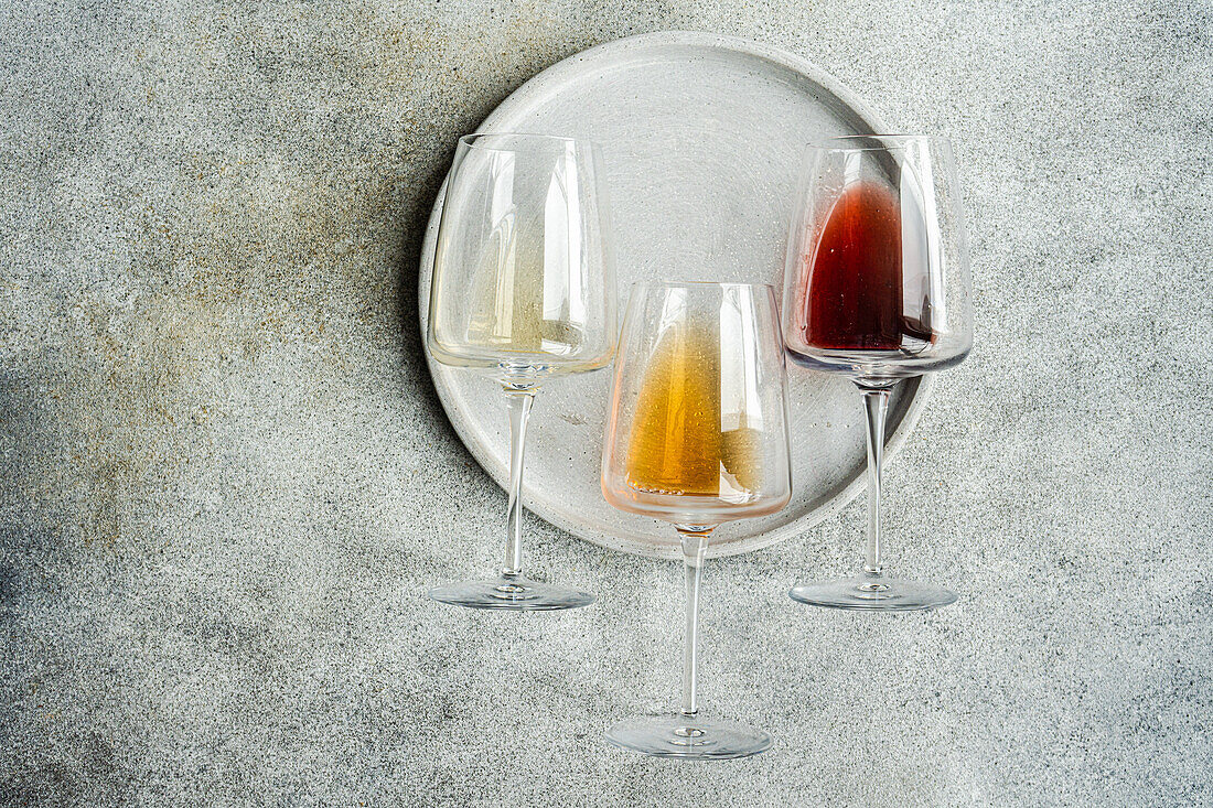 High angle of three varieties of Georgian dry wine glasses (white, amber and red) lying on a plate on concrete grey table