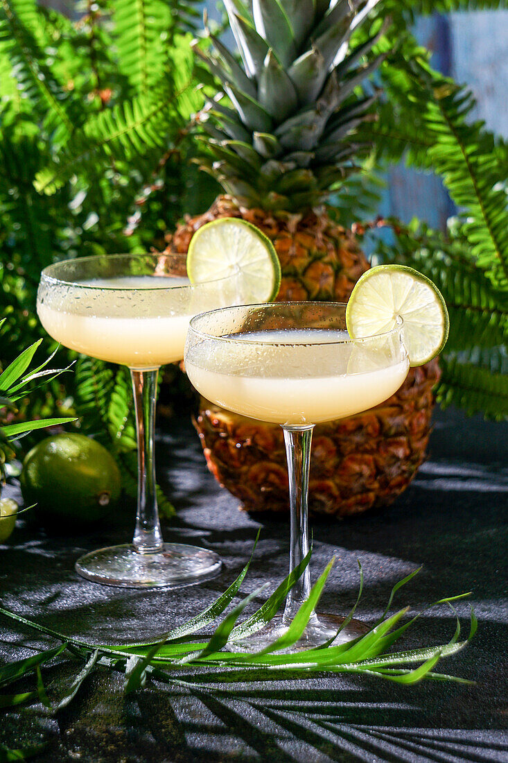 Summer cocktail pineapple daiquiri with vodka, pineapple juice, frozen motion and flying drops. Tropical background with palm leaves