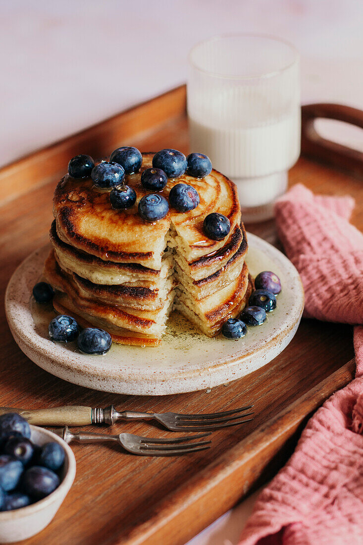 Pfannkuchenstapel auf einem Tablett mit frischen Blaubeeren und Sirup und einem Glas Milch