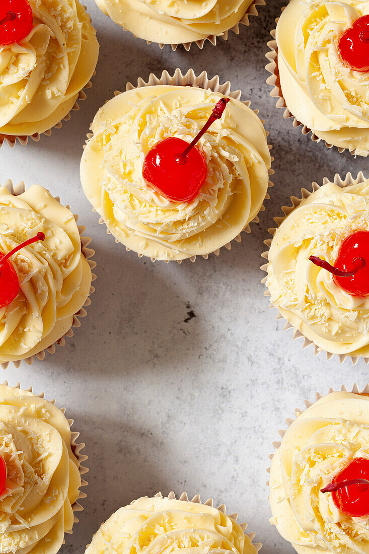 Törtchen mit Buttercreme-Glasur, geriebener weißer Schokolade und Maraschino-Kirschen mit Stielen