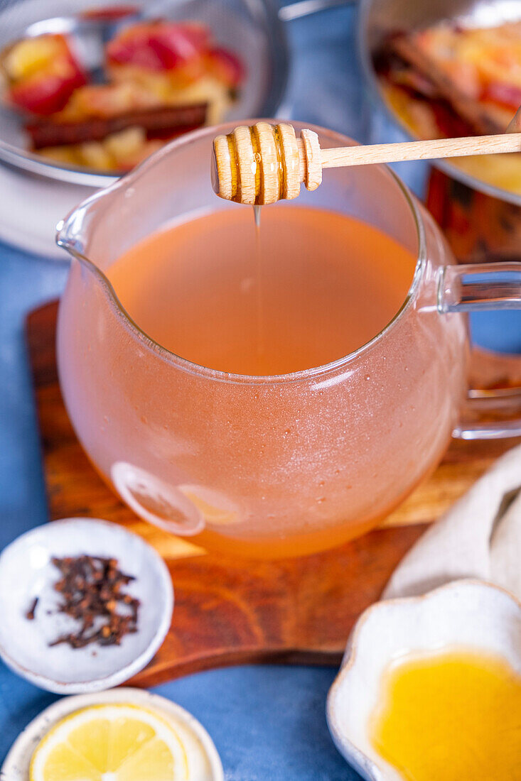Honig wird in Apfeltee in einer gläsernen Teekanne getropft, Nelken, Apfelscheiben drum herum