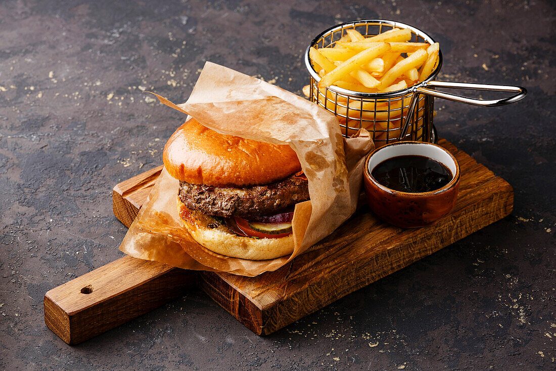 Burger with meat and fries in a serving basket on a dark background