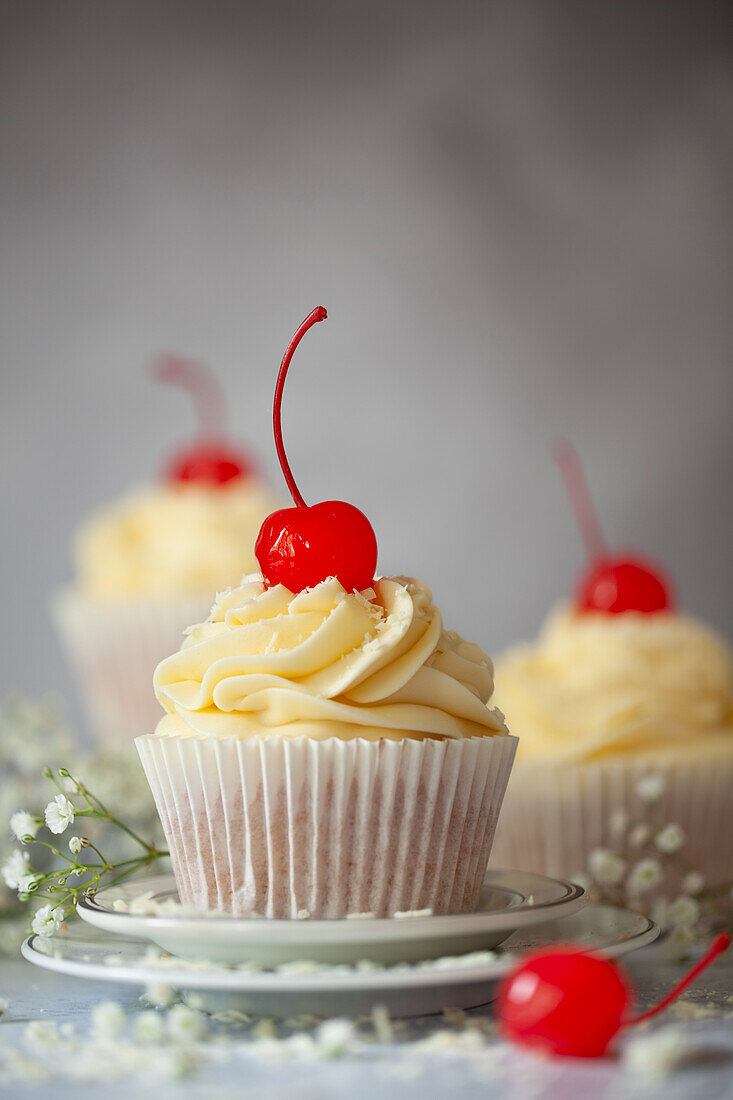 White chocolate cupcakes with piped white chocolate buttercream, grated white chocolate and maraschino cerries. topped with buttercream, grated white chocolate and stemmed maraschino cherries
