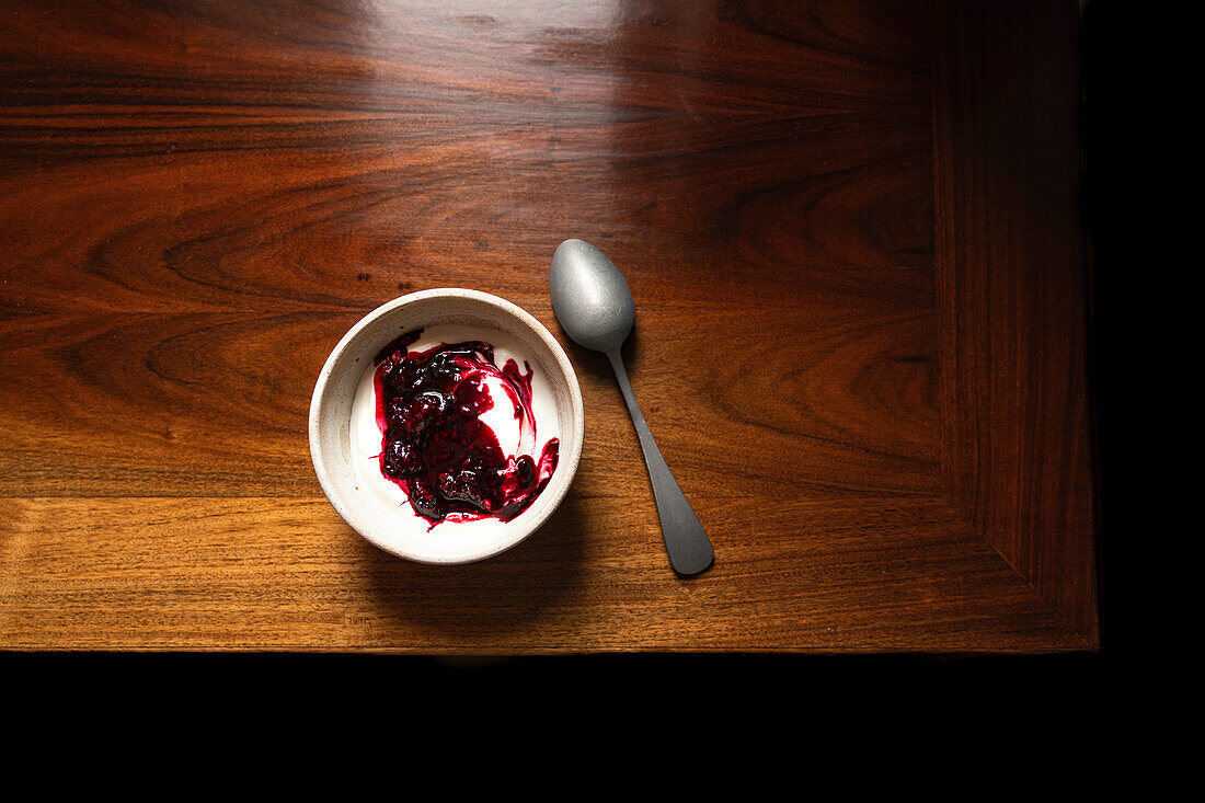 Bowl of yoghurt and blackberry compote on antique wooden table with silver spoon