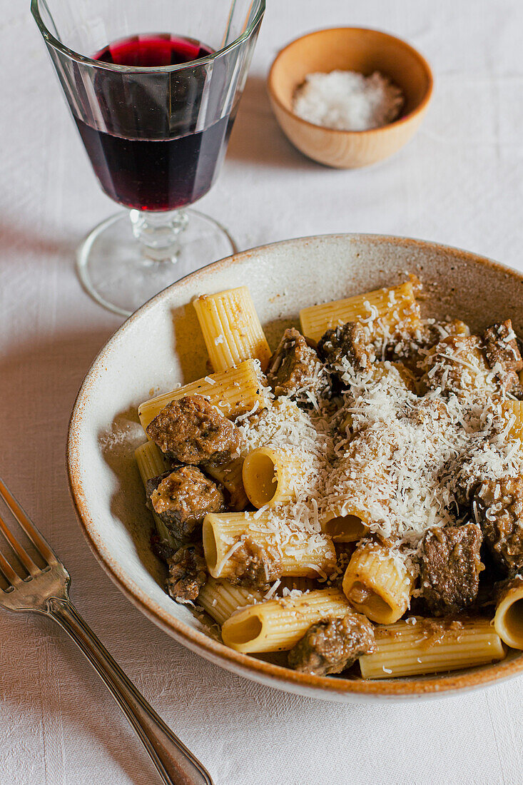 Bowl of pasta, meat and cheese, served with a glass of wine