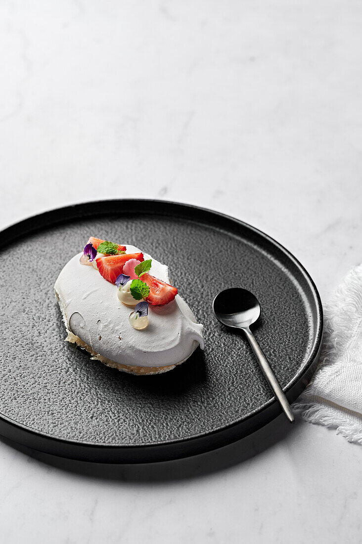 Meringue with yoghurt mousse, macerated strawberries and bergamot gel on a black plate