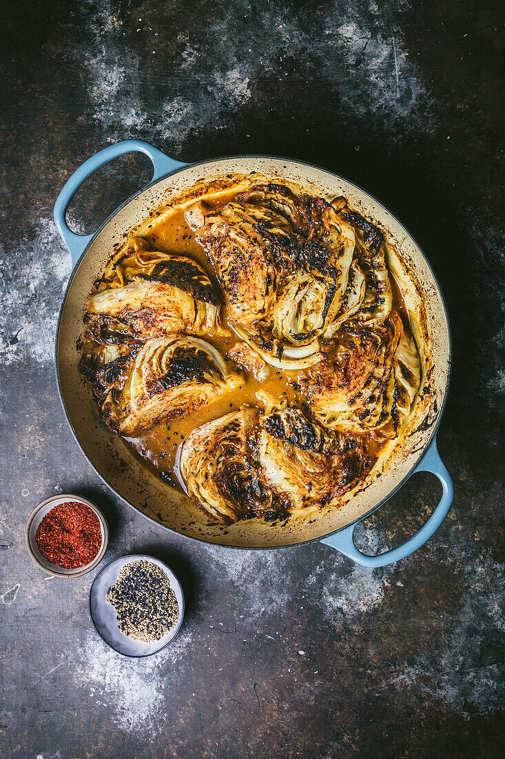 Braised cabbage wedges in a casserole with sauce and chilli and sesame garnish