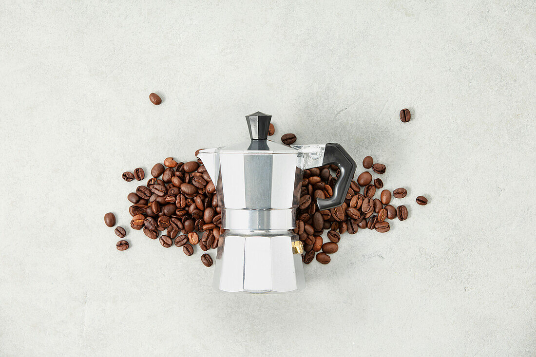 Moka pot coffee machine and coffee beans on a grey stone background