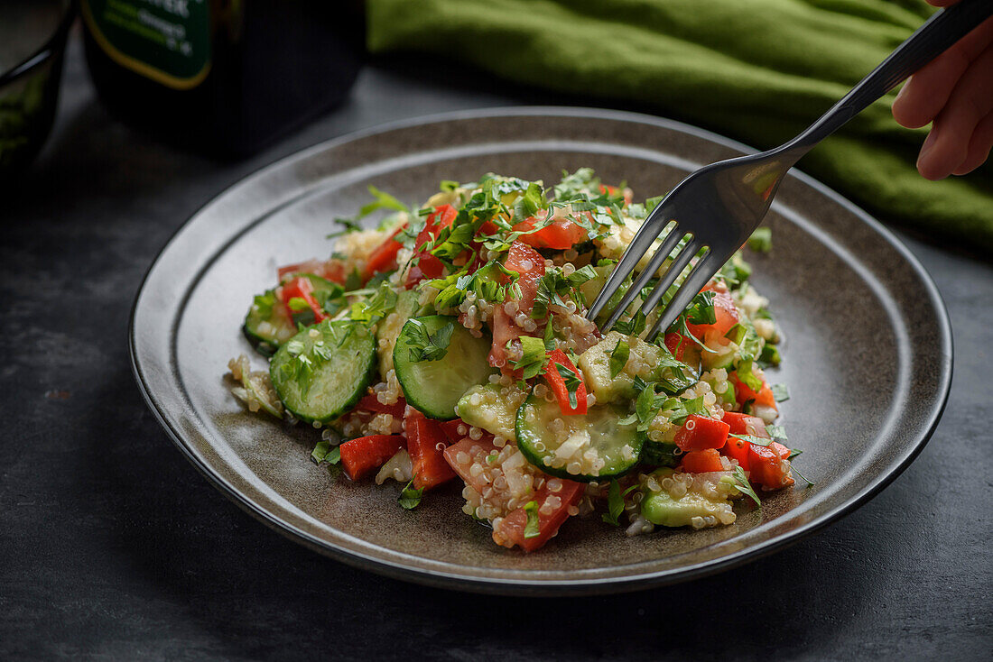 Quinoa and vegetable salad. A human hand selects a salad with a fork